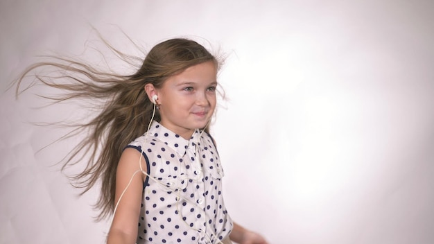 Kind mit Ohrenklappen, die im Studiohintergrund tanzen Das Mädchen hört Musik auf dem Smartphone