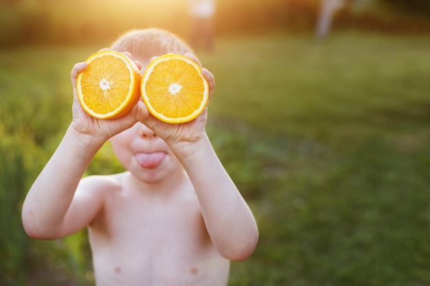 Kind mit Orangenhälften auf den Augen glückliches Kind, das Spaß hat und Zunge zeigt