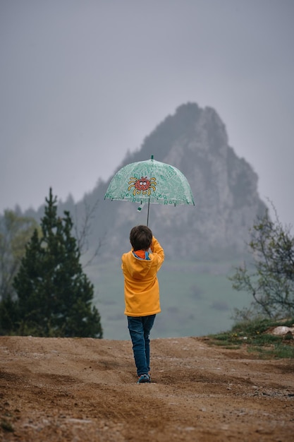 Kind mit Regenschirm und gelber Jacke