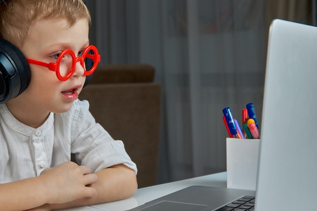 Kind mit roter Brille und Kopfhörern hat Spaß bei der Kommunikation per Videoverbindung mit einem Laptop