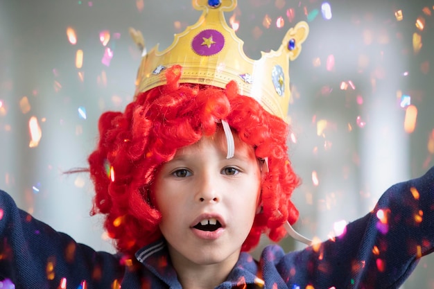 Kind mit roter Perücke und Krone Clown-Junge mit glänzenden Bonbons