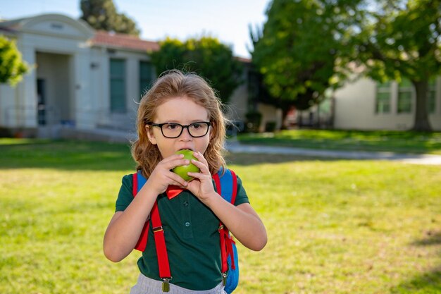 Kind mit Rucksäcken im Schulpark Schüler mit Rucksäcken im Freien Schüler isst Apfel