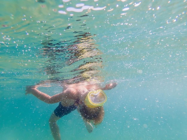 Kind mit Schnorchelmaske, das unter Wasser im Meer taucht