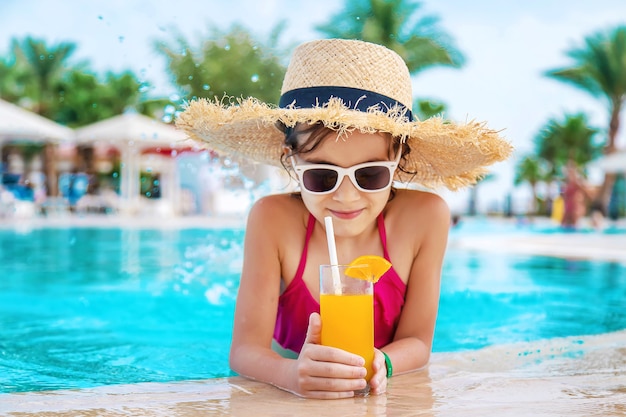 Kind mit Strohhut trinkt einen Cocktail am Pool