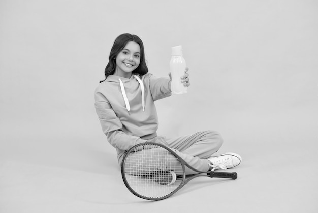 Kind mit Tennisschläger Teenager-Mädchen trinkt Wasser nach dem Sporttraining Badmintonspieler entspannen sich gesund und aktiver Lebensstil glückliche Kindheit hydratisiertes Kind sitzen mit Schläger und Wasserflasche