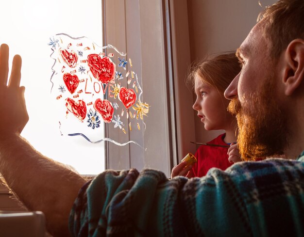 Kind mit Vater malt Liebesschild, spielt drinnen, Quarantäne, Familienfreizeit, Valentinstag, zu Hause bleiben, Kunstspaß