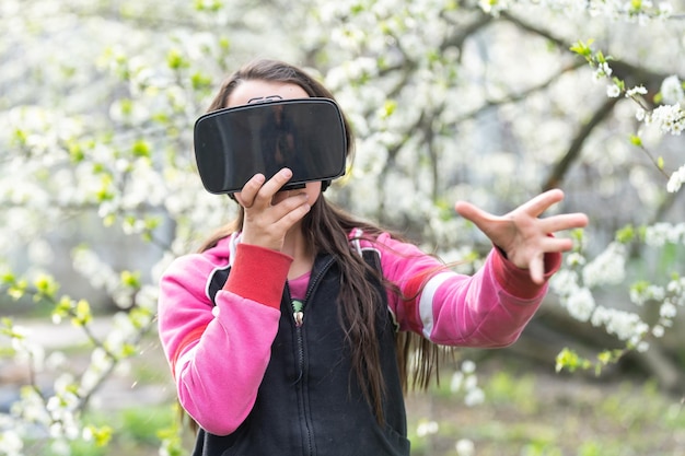 Kind mit Virtual-Reality-Headset, das zu Hause hinter natrue im Freien sitzt.