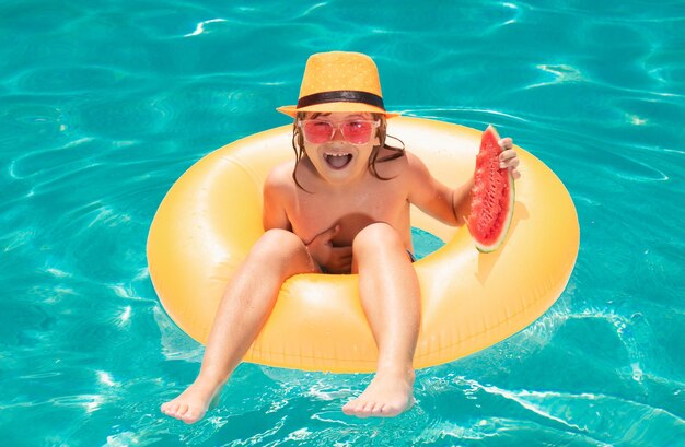 Kind mit Wassermelone schwimmt mit aufblasbarem Ring im Schwimmbad eines tropischen Resorts für Kinder