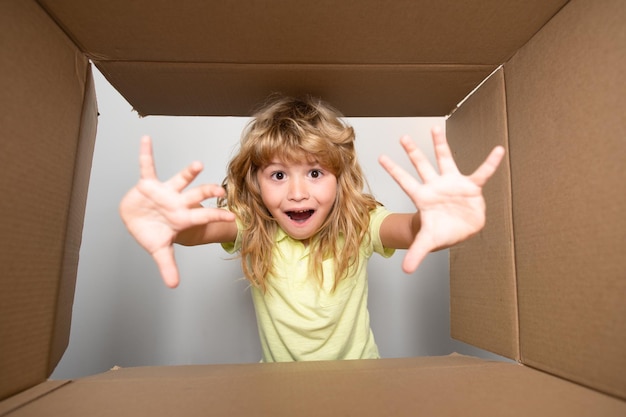 Kind öffnet Karton und zieht Geschenk daraus Kleiner Junge, der in Paketbox schaut und sich freut, eine Überraschung zu erhalten Junges Kind, das Freude auf seinem Gesicht zeigt Auspacken Karton für Kinder