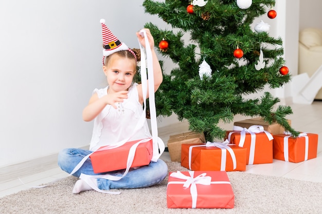 Kind öffnet Weihnachtsgeschenke. Kind unter Weihnachtsbaum mit Geschenkboxen.