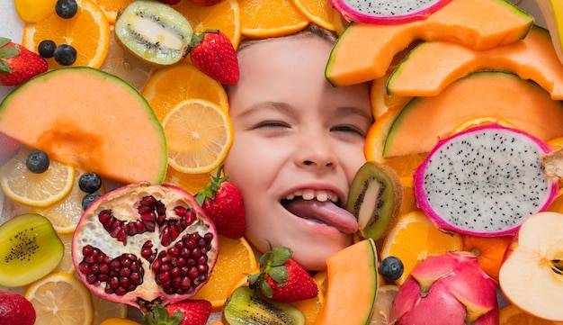 Kind probiert Obst, leckt lustig Obst, Draufsicht auf Fynny-Kindergesicht mit verschiedenen Früchten, Sommerfrüchten