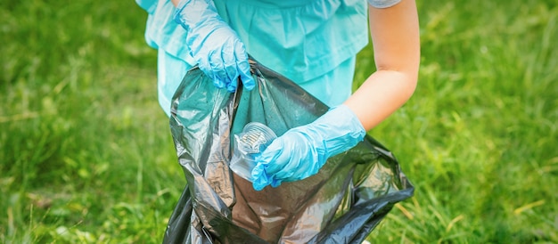 Kind sammelt Plastikmüll vom Gras, das Müll in Müllsack im Park wirft