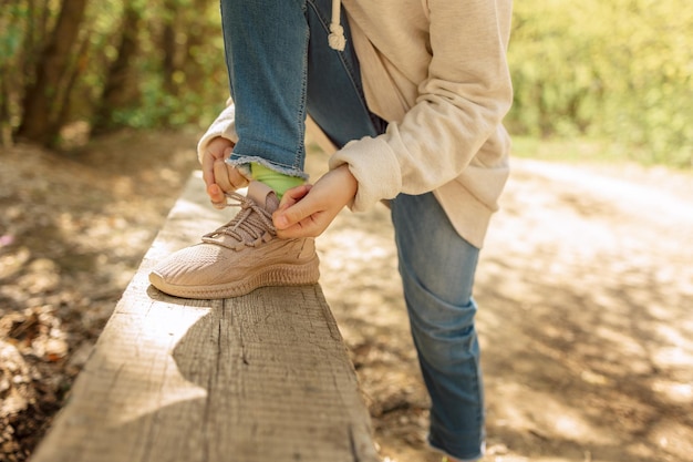 Kind schnürt seine Turnschuhe im Frühlingspark für einen Spaziergang. Mädchen bindet Schleife an ihrem Schuh im Freien. Gesundheit