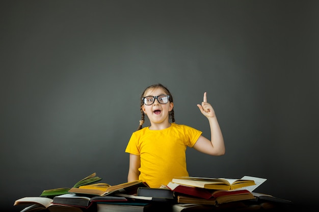 Kind Schulmädchen zeigt Tafel auf Schreibtisch drinnen, Schreibtisch Stapel Bücher