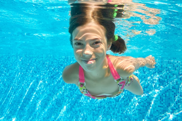 Kind schwimmt im Pool unter Wasser, glückliches aktives Mädchen taucht und hat Spaß im Wasser, Kindereignung und Sport auf Familienferien
