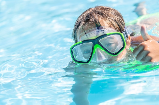 Kind schwimmt in einem Pool mit Schutzbrille beim Zeigen von Daumen nach oben Geste.