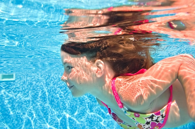 Kind schwimmt unter Wasser im Schwimmbad gesundes aktives kleines Mädchen taucht und hat Spaß unter Wasser