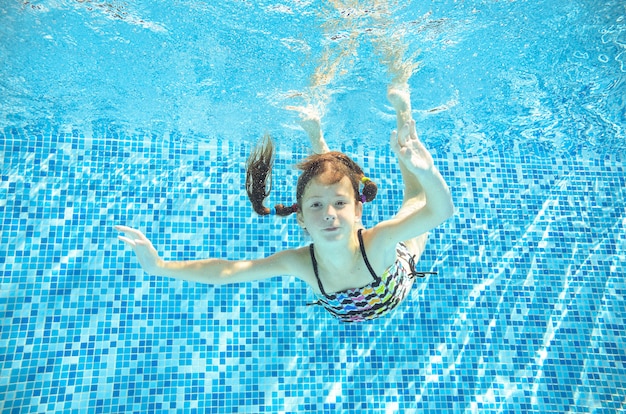 Kind schwimmt unter Wasser im Swimmingpool, glückliches aktives Jugendlichmädchen taucht und hat Spaß unter Wasser, Kindereignung und Sport auf Familienurlaub auf Erholungsort