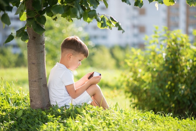 Kind sitzt auf dem Gras und schaut am Telefon