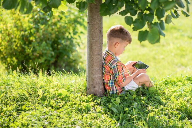 Kind sitzt auf dem Gras und schaut am Telefon