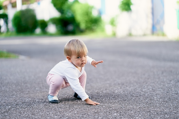 Kind sitzt auf den Hinterbeinen auf dem Asphalt und berührt es mit der Hand