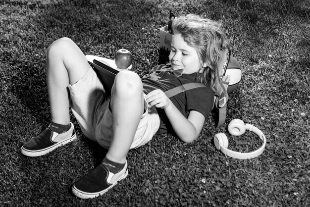 Kind sitzt auf Gras mit Tablet im Park Outdoor-Schule lächelnder Junge hält Tablet-Computer-Schule