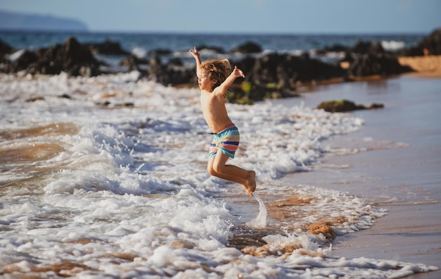 Kind spielt am Ozeanstrand Kind springt in die Wellen am Meer Urlaub kleiner Junge läuft auf tropisch