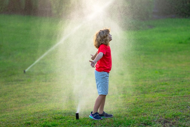 Kind spielt im Sommer im Hinterhof, Wasserspaß im Garten, Kind spielt mit Wassersprinkler im Garten, lustig l