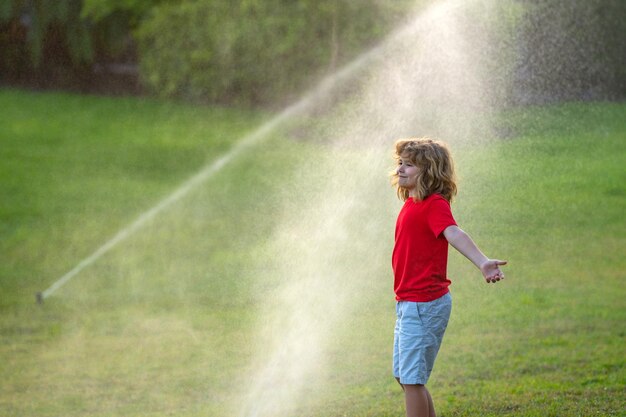 Kind spielt im Sommer im Hinterhof, Wasserspaß im Garten, Kind spielt mit Wassersprinkler im Garten, lustig l