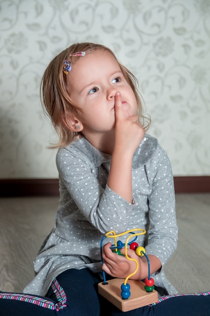 Kind spielt mit Labyrinth. Kleines Mädchen, das mit einem Finger nahe dem Mund denkt. Pädagogisches Spielzeug.