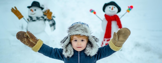 Kind spielt mit Schnee im Park auf weißem Schneehintergrund glückliches Kind spielt mit Schneeball gegen W...