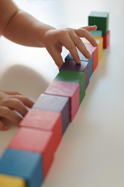 Kind spielt und baut mit bunten Holzspielzeugziegeln auf weißem Holztisch Frühes Lernen