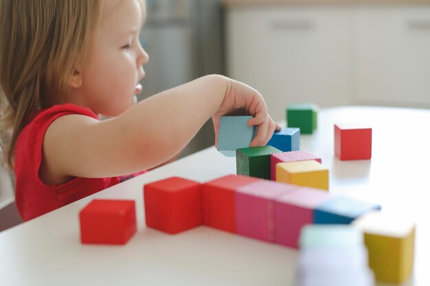 Kind spielt und baut mit bunten Holzspielzeugziegeln auf weißem Holztisch Frühes Lernen