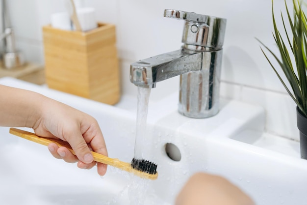 Kind spült Bambuszahnbürsten mit Wasser, das aus dem Wasserhahn des Waschbeckens läuft