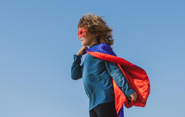Kind trägt ein Superhelden-Kostüm Superhelden-Kind vor blauem Sommerhimmel Hintergrund Kind hat Spaß