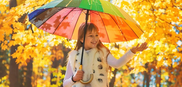 Kind unter einem Regenschirm im Herbstpark Selektiver Fokus