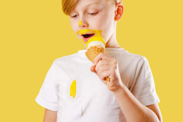 Kind verschüttet Eis. Kleidung ruiniert. Ein Junge, der Bananeneis auf gelbem Hintergrund isst