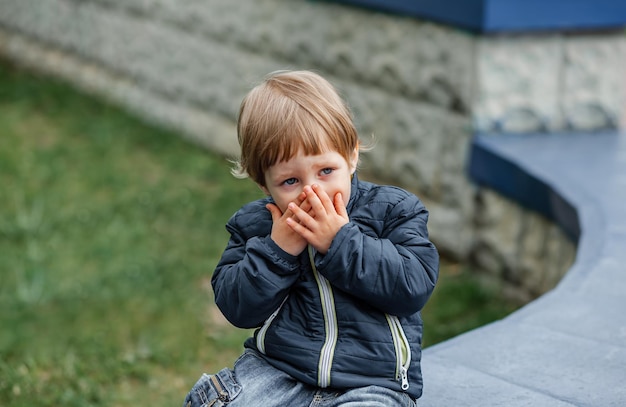 Foto kind versteckt sich hinter seinen handflächen. verärgertes kind, das zu hause sein gesicht bedeckt