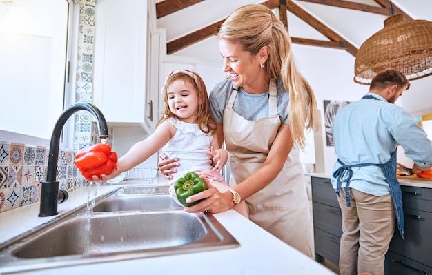 Kind wäscht Gemüse und kocht mit Mutter zusammen mit gesunder Ernährung und Ernährung zum Mittagessen, Abendessen und Salat Mädchen hilft Mutter, Pfeffer bei fließendem Wasser im Haus der Familie zu reinigen