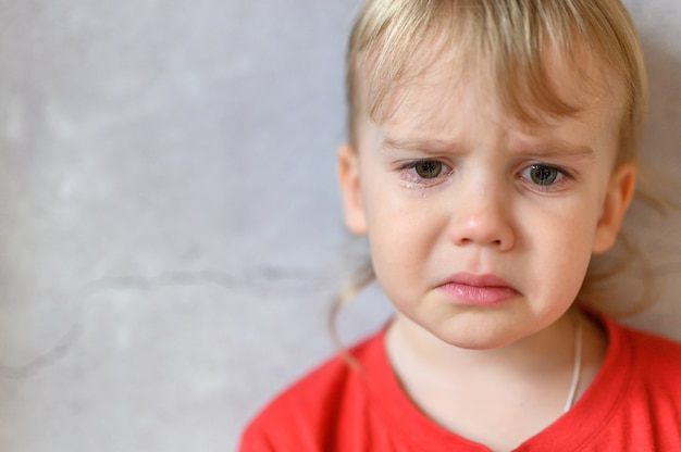 Kind weint. das Gesicht eines niedlichen kleinen verärgerten vierjährigen Jungen in Tränen. Trauer der Kinder. grauer Betonwandhintergrund. Platz für Text