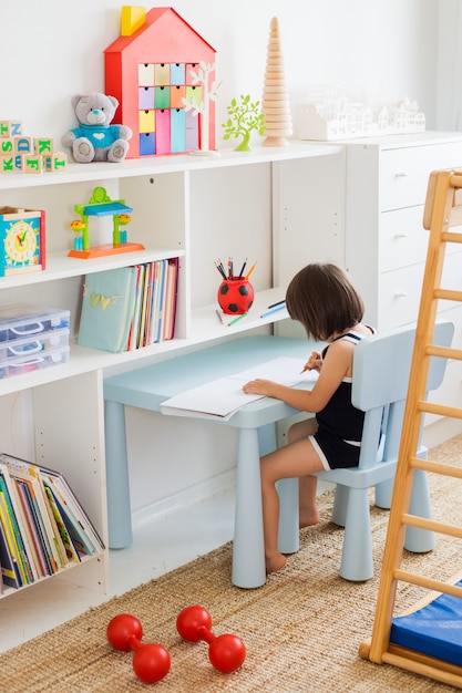 Kind zeichnet mit Bleistiften, die am Tisch im Kinderzimmer sitzen.