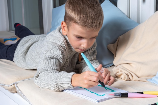 Kind zeichnet mit Filzstiften auf Papier, liegt auf dem Boden. Kind macht zu Hause Schulunterricht. Bildung