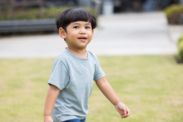 Kind zu Fuß auf dem Rasen Asiatischer kleiner Junge trägt ein blaues Hemd, das herumläuft Kinder spielen auf dem Spielplatz mit Sonnenlicht