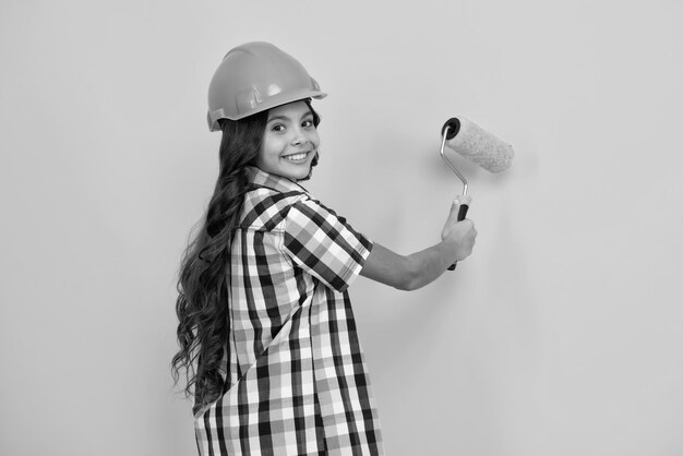 Foto kindbauer in helm jugendliche malerin mit malpinselwerkzeug oder malrolle kind auf reparaturarbeiten isoliert auf gelben hintergrund kinder renovierungskonzept
