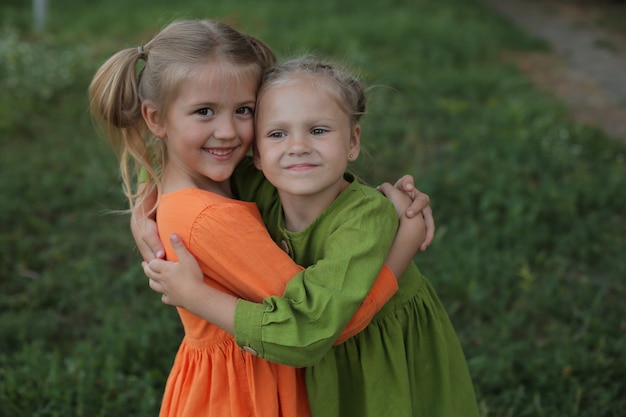 Kinder blonde Mädchen in einem gelben und grünen Kleid umarmen sich vor dem Hintergrund eines Freundesgartens