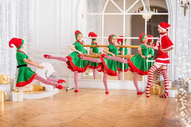 Kinder, die als Elfen verkleidet sind und in einer Ballettscheune üben, betrachten eine tanzende Ballerina, die als Weihnachtsmann in einem geräumigen weißen Studio verkleidet ist.