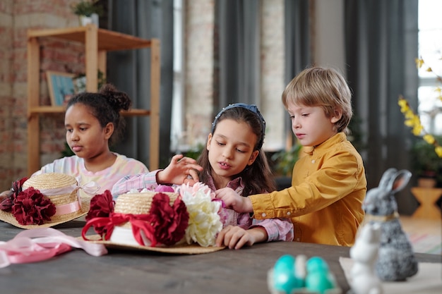 Kinder, die am Tisch sitzen und im Team arbeiten, schmücken gemeinsam Hüte mit Blumen für den Urlaub