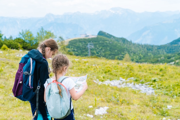 Kinder, die an einem schönen Sommertag in den Alpenbergen Österreich wandern, ruhen auf Felsen. Kinder betrachten Karte Berggipfel im Tal.