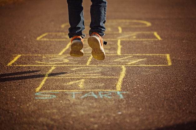 Foto kinder, die draußen hopse auf spielplatz spielen. hopscotch beliebtes straßenspiel