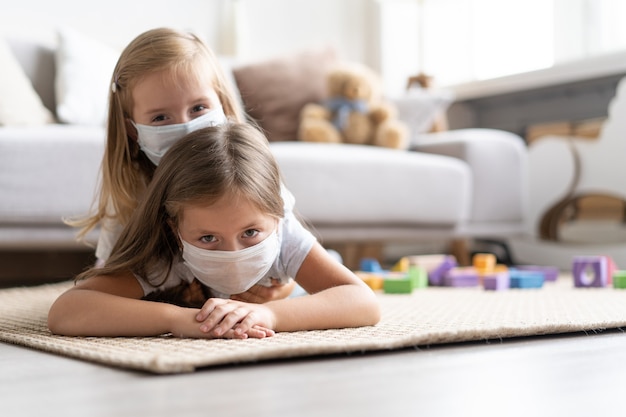 Kinder, die eine Maske zum Schutz von Covid-19 tragen und im Wohnzimmer spielen. Bleiben Sie zu Hause unter Quarantäne, um eine Coronavirus-Pandemie zu verhindern